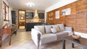 Un salon chaleureux avec un canapé, un mur en bois et une cuisine en arrière-plan.
