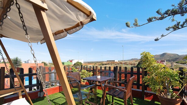 En terrasse med gyngestativ, udendørs bord og stole samt en potteplante.