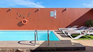En swimmingpool med rød væg, gelændere i metal og liggestole.