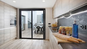 A modern kitchen with a sliding glass door leading to a dining area, stainless steel appliances, and a wooden countertop with food items. - Villa Dolce Vita Tenerife Sur with Sea Views, Private Pool, Terraces, and Wi-Fi (Adeje)