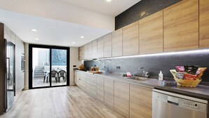 A modern kitchen with wooden cabinets, a built-in dishwasher, and a glass door leading to a dining area. - Villa Dolce Vita Tenerife Sur with Sea Views, Private Pool, Terraces, and Wi-Fi (Adeje)