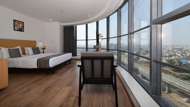 A modern hotel room with a large bed, a wooden floor, a desk with a chair, and a large window offering a city view. - Ginger Ahmedabad RTO Circle (Ahmedabad)