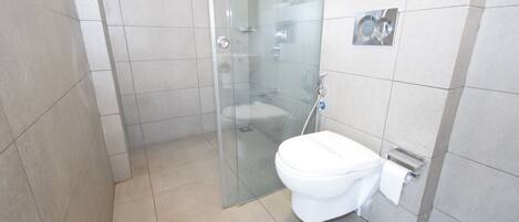 Une salle de bain moderne avec une douche à parois de verre, des toilettes blanches et un distributeur de serviettes fixé au mur.