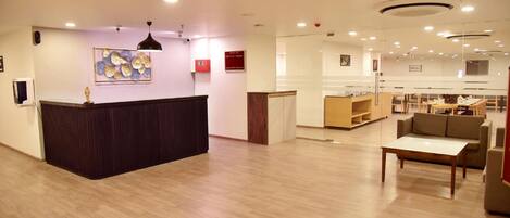 A spacious lobby with a reception desk, seating area, and a kitchen in the background.