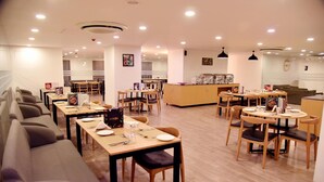 A modern restaurant with multiple dining areas, including a long communal table and several smaller tables with chairs. - Ginger Ahmedabad RTO Circle (Ahmedabad)