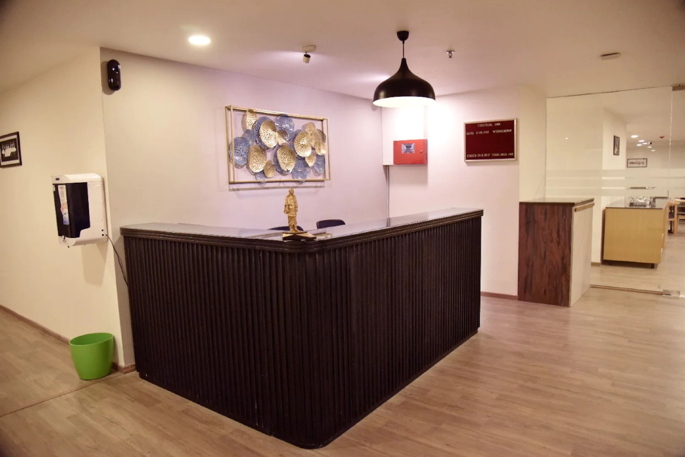 A reception desk with a framed artwork above it, a red sign with text, and a green trash bin to the left.