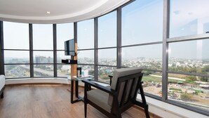 A modern room with a curved ceiling, large windows offering a city view, a wooden floor, a desk with a chair, and a flat-screen TV. - Ginger Ahmedabad RTO Circle (Ahmedabad)