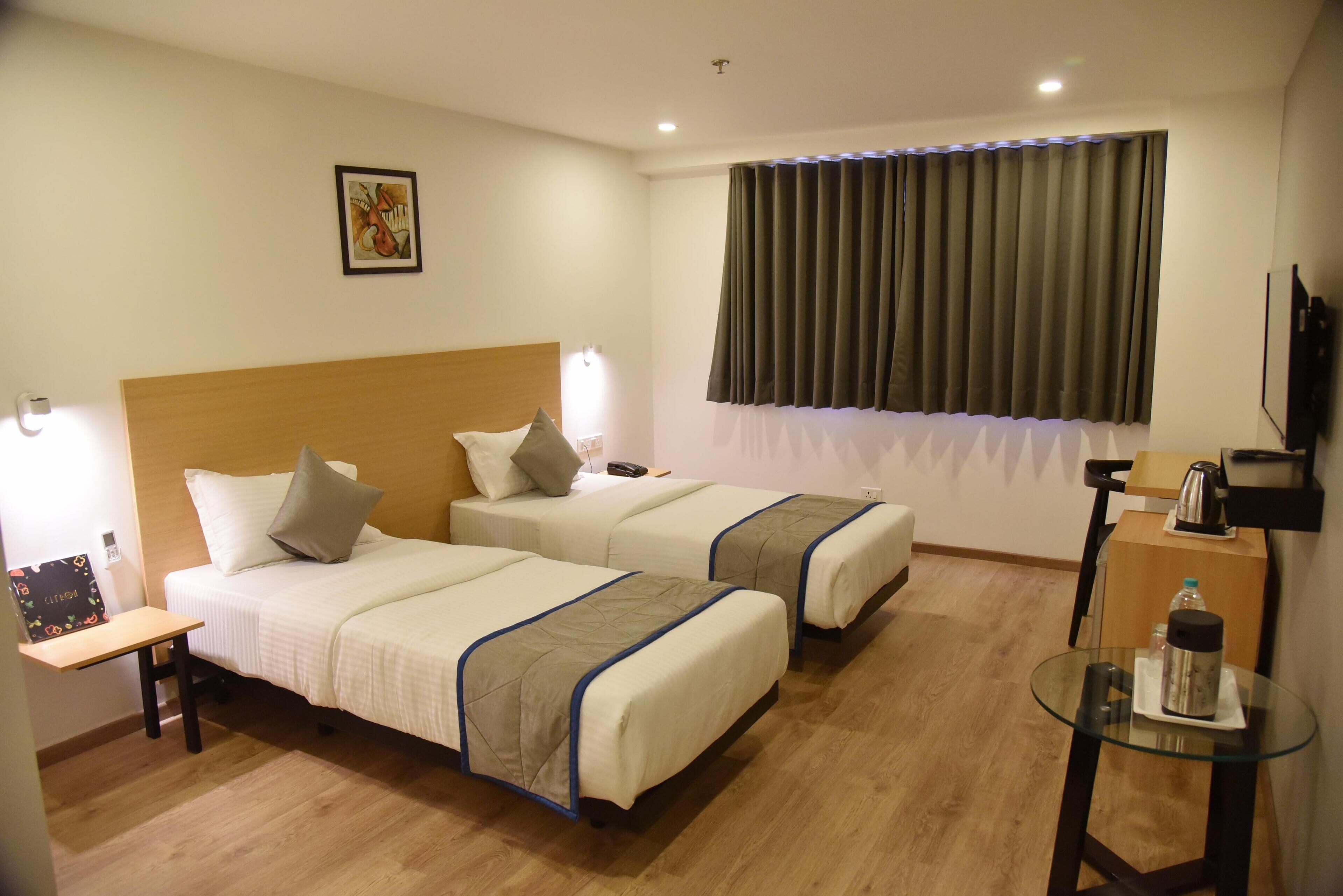 A hotel room with two beds, a small desk, a glass table, a television, and a window with curtains.