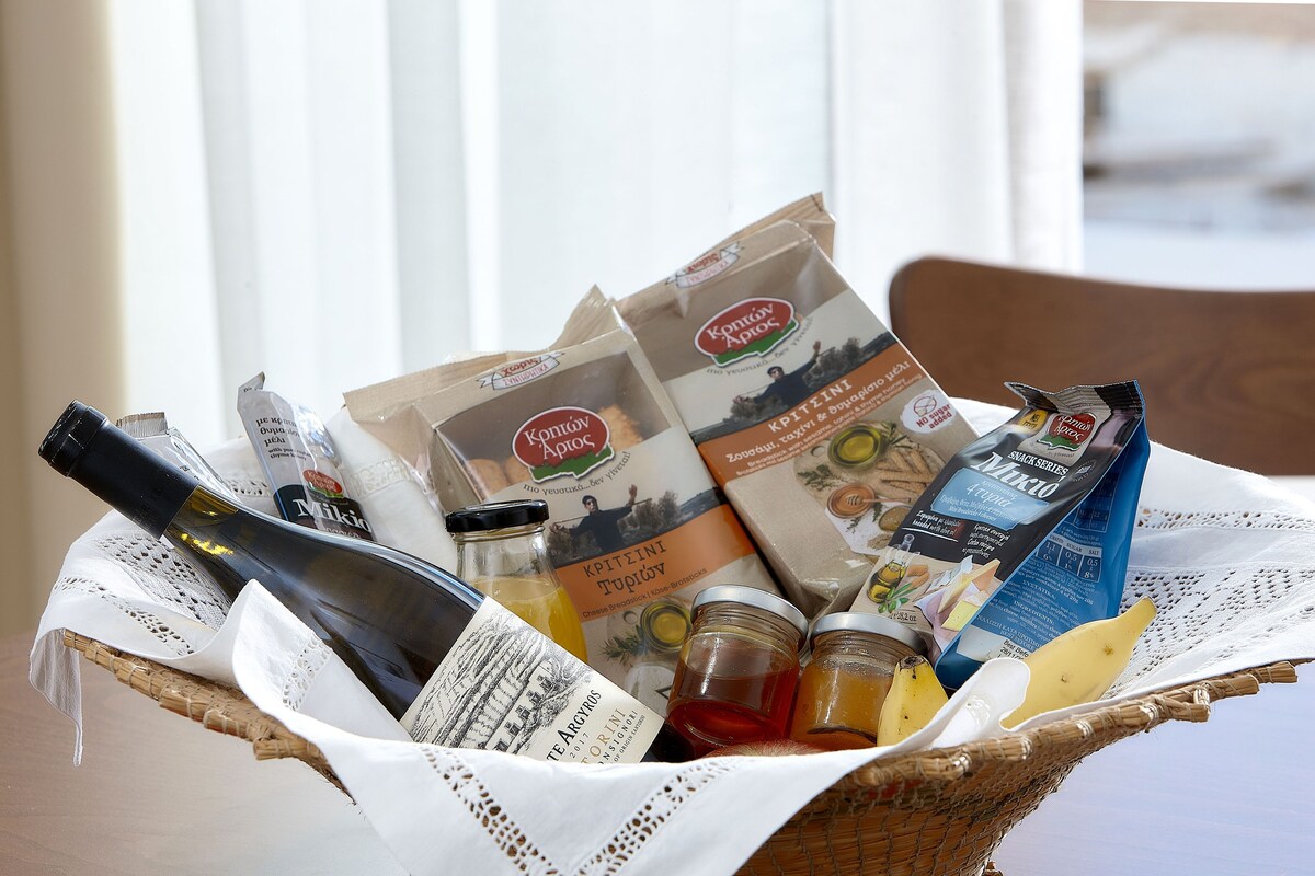 Ein Korbkorb, gefüllt mit verschiedenen Lebensmitteln, darunter eine Weinflasche, Gläser mit Konfitüre und verpackten Produkten.