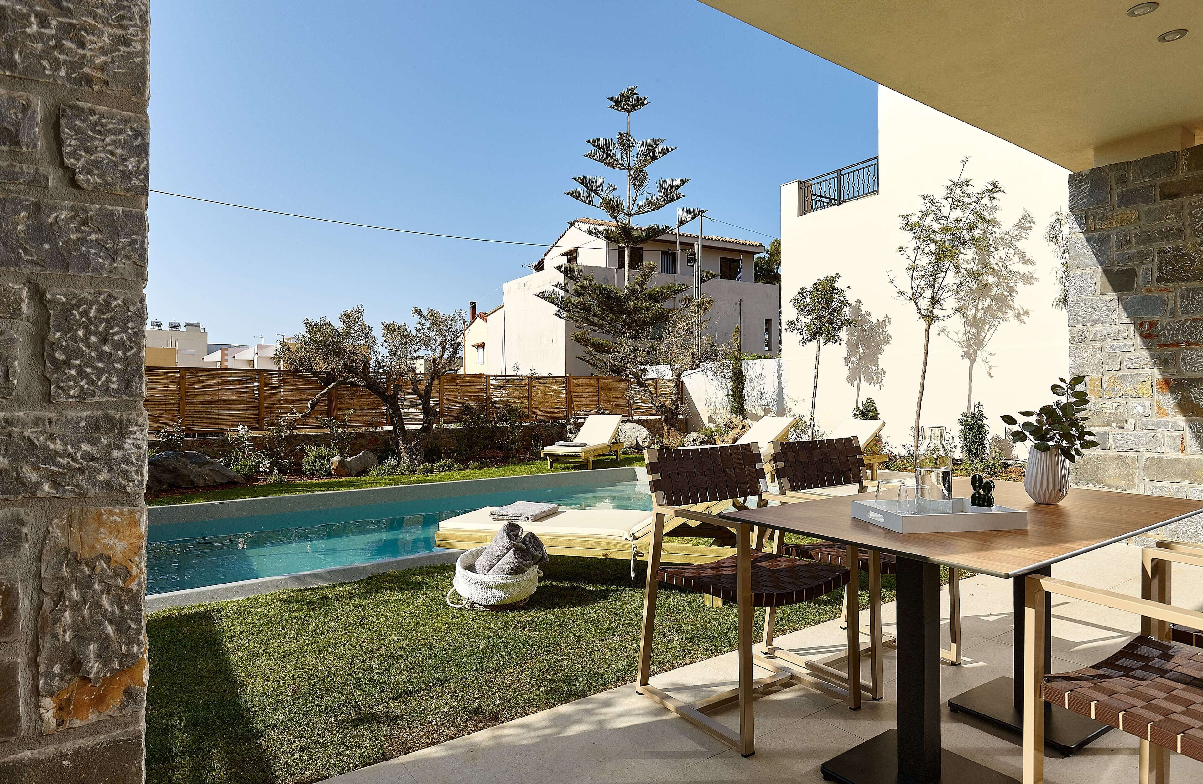 A poolside area with a wooden table, chairs, and a stone wall.
