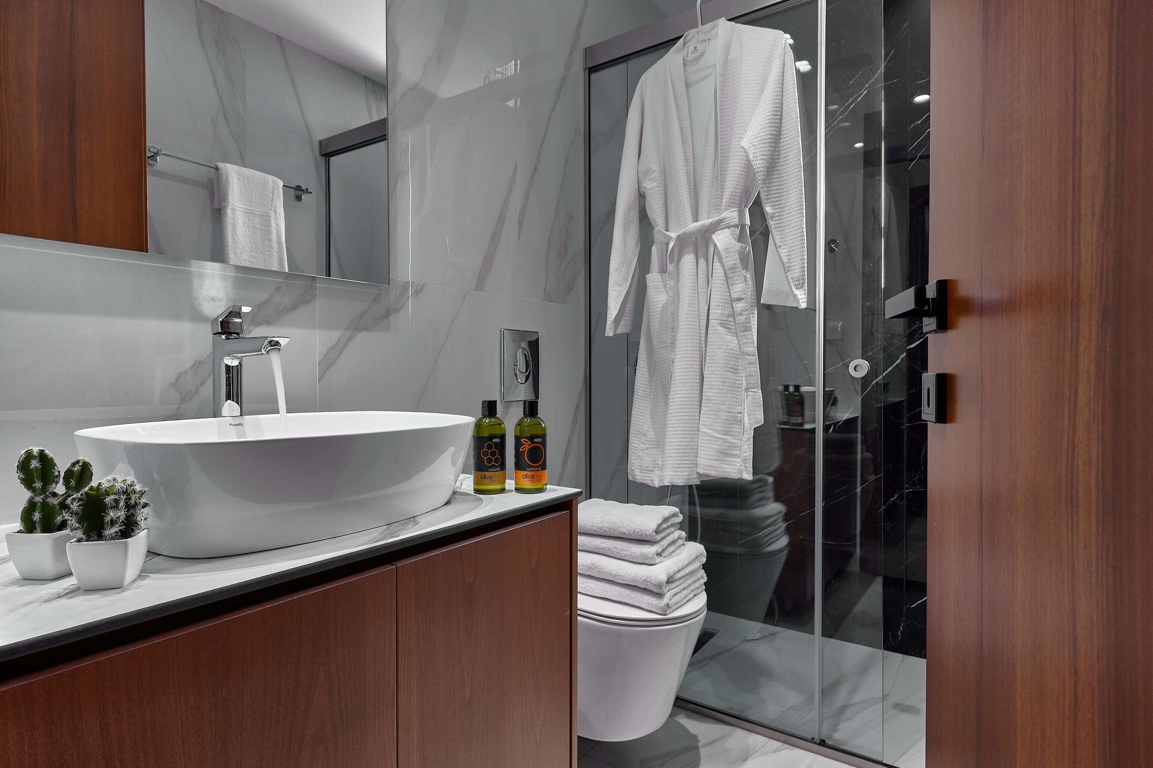 A modern bathroom with a large white sink, two potted plants, and a glass shower enclosure.