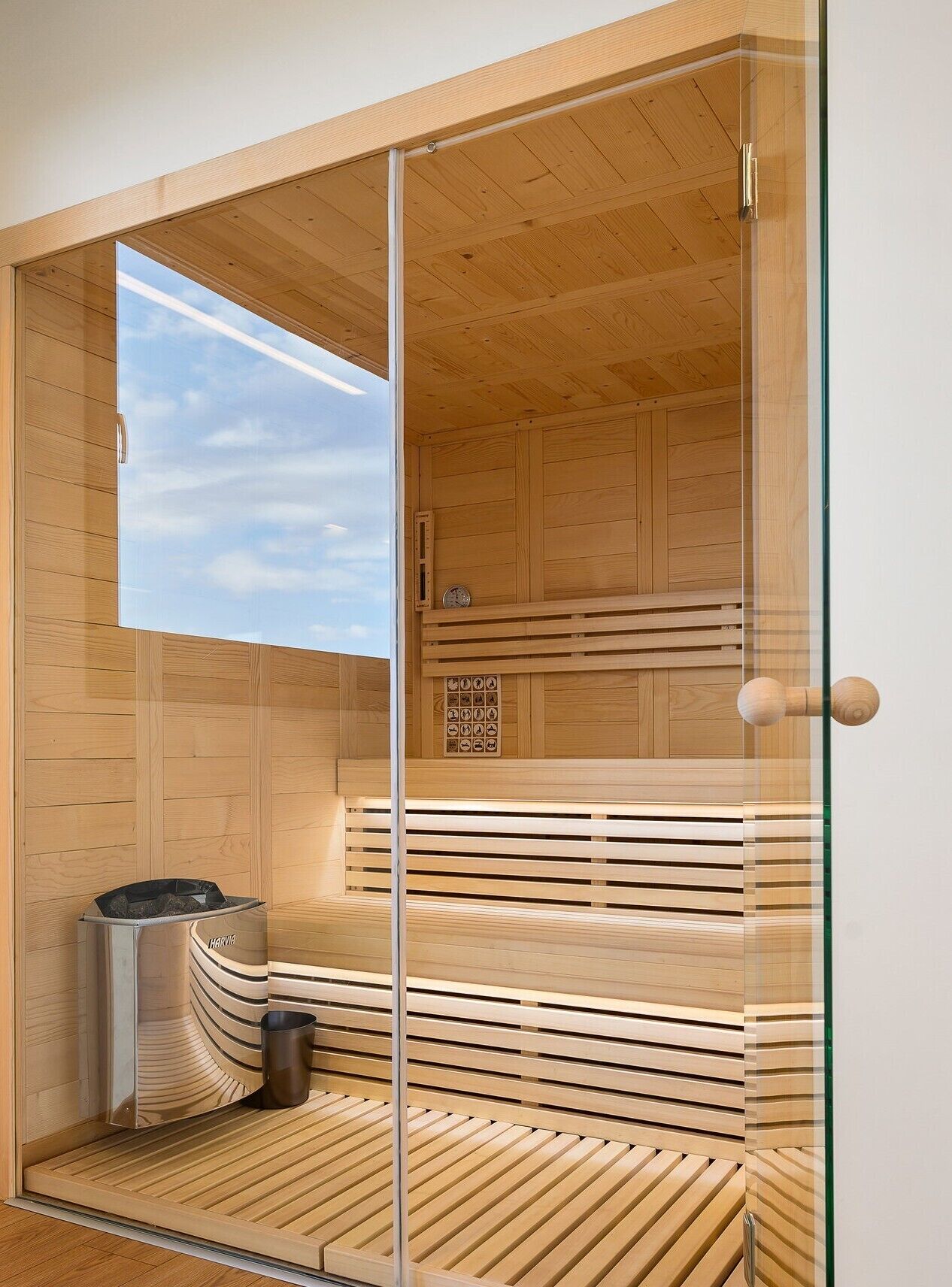 Een sauna met houten wanden en een glazen deur, een bankje en een kleine prullenbak.