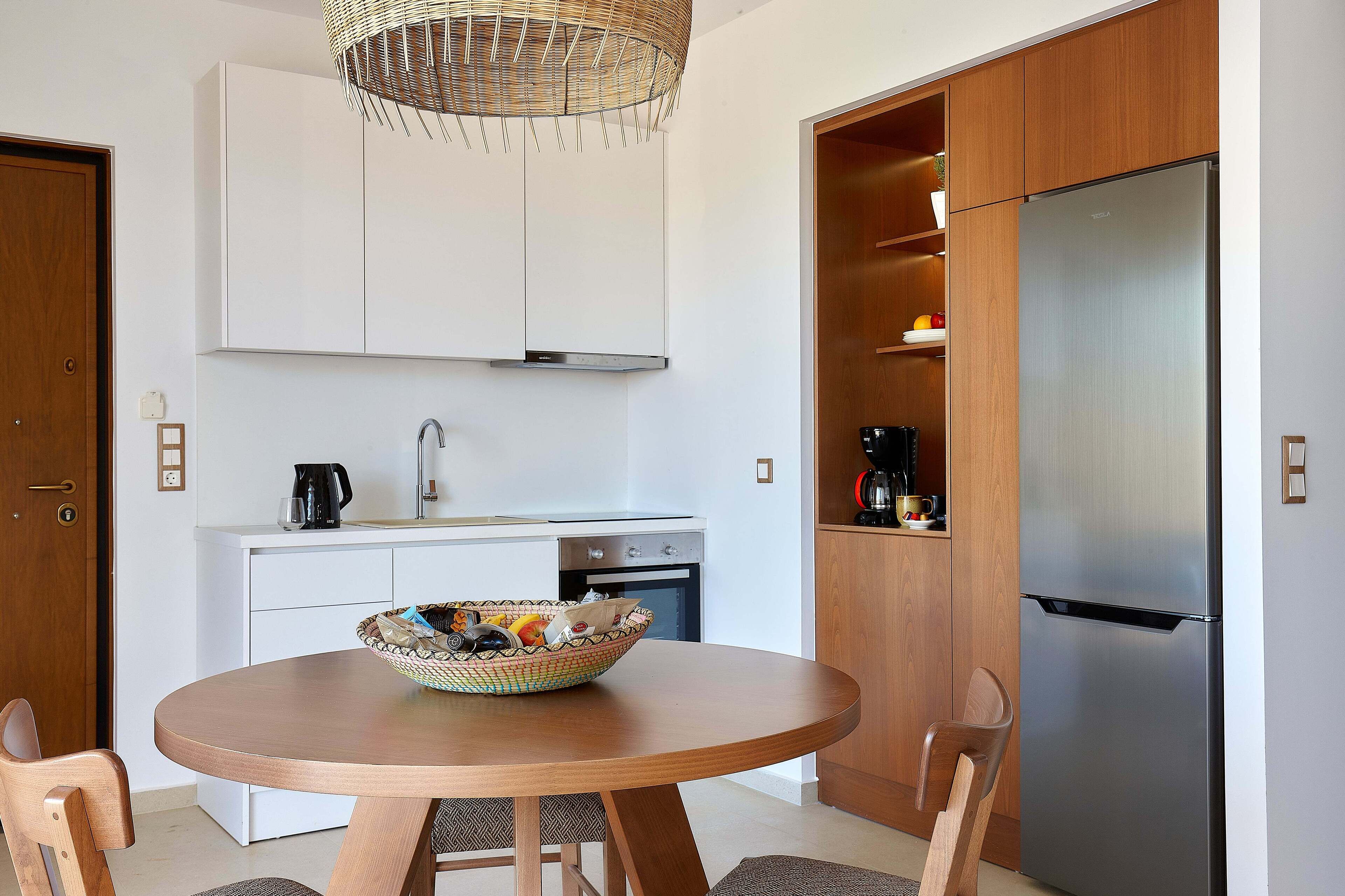 A modern kitchen with white cabinets, a stainless steel refrigerator, and a round wooden table with chairs.