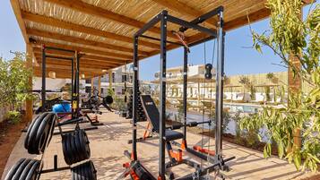 An outdoor gym with weightlifting equipment, a covered wooden structure, and a pool in the background.