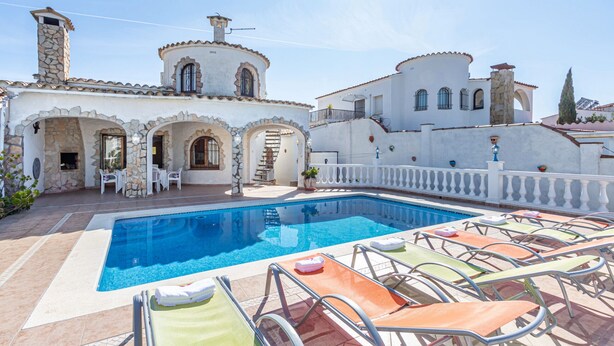 A pool area with lounge chairs, a stone building with arched doorways, and a clear blue sky. - 0038-CREUS  House at the canal with pool and mooring (Empuriabrava)