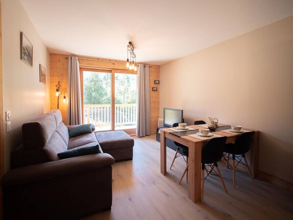 Een gezellige woonkamer met een bank, een eettafel met stoelen, een televisie en een balkon met gordijnen.