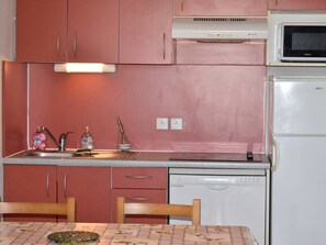 Una cocina compacta con armarios rosados, microondas, lavavajillas y una mesa con sillas.