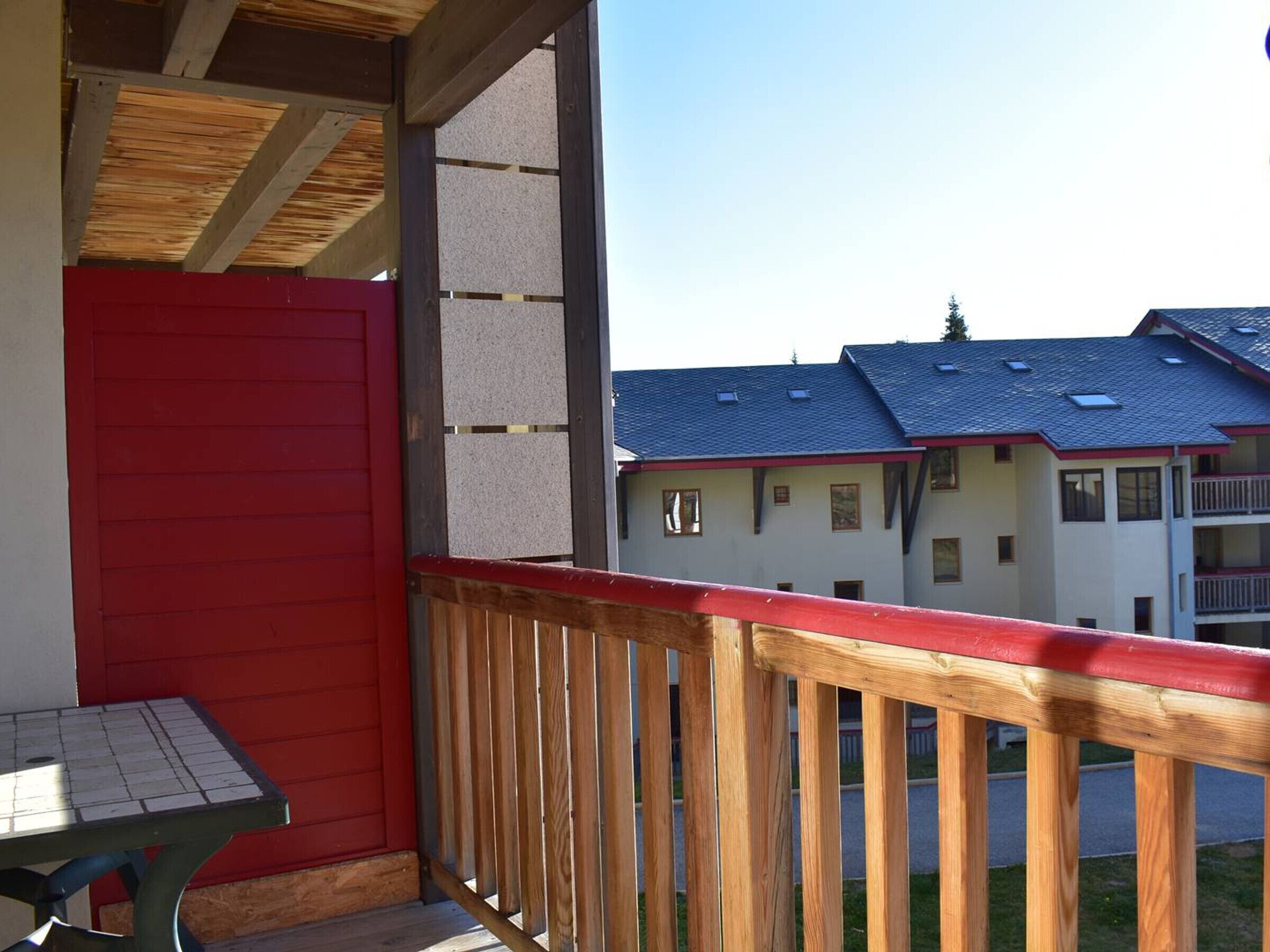 A balcony with a red door and a table, overlooking a row of white buildings with blue roofs.