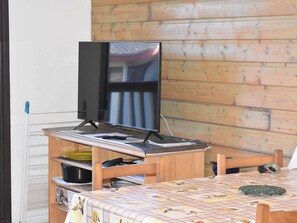 Quarto com parede de madeira, televisão em um suporte, mesa com toalha de mesa estampada e uma cadeira.