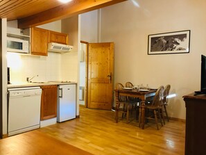 A compact kitchen with wooden cabinets, a microwave, a dishwasher, and a dining area with a table and chairs.