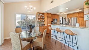A modern kitchen with wooden cabinets, stainless steel appliances, and a glass dining table with wicker chairs. - PGA West 3Bed Golf Mountain and Course View Home (La Quinta)