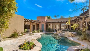 A pool surrounded by a patio area with stone flooring and potted plants.