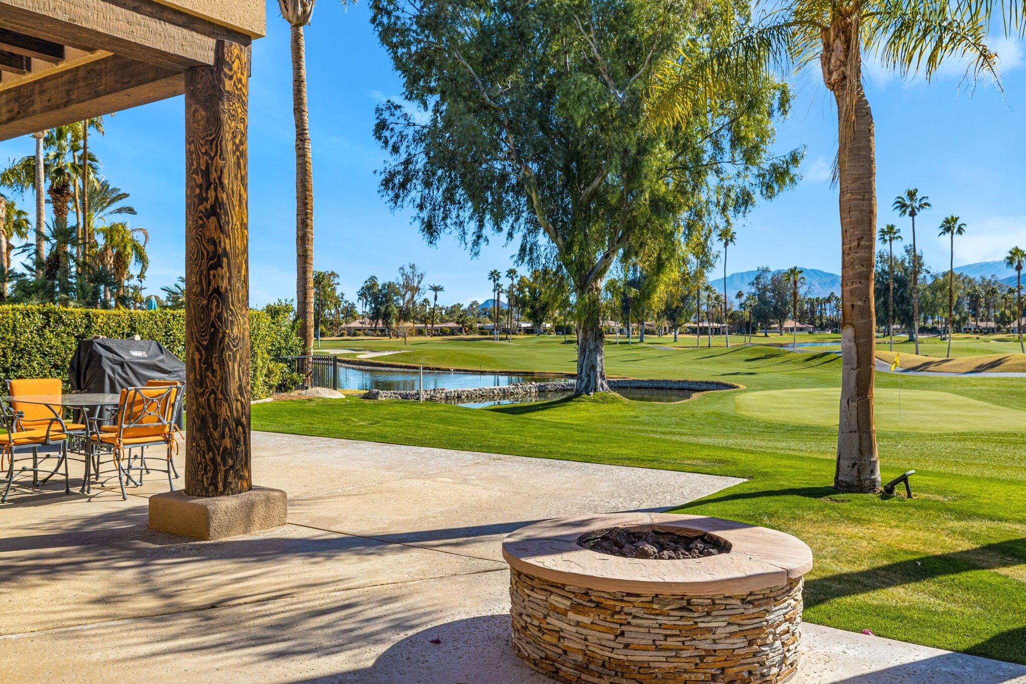 A patio area with outdoor seating, a stone fire pit, and a view of a golf course.