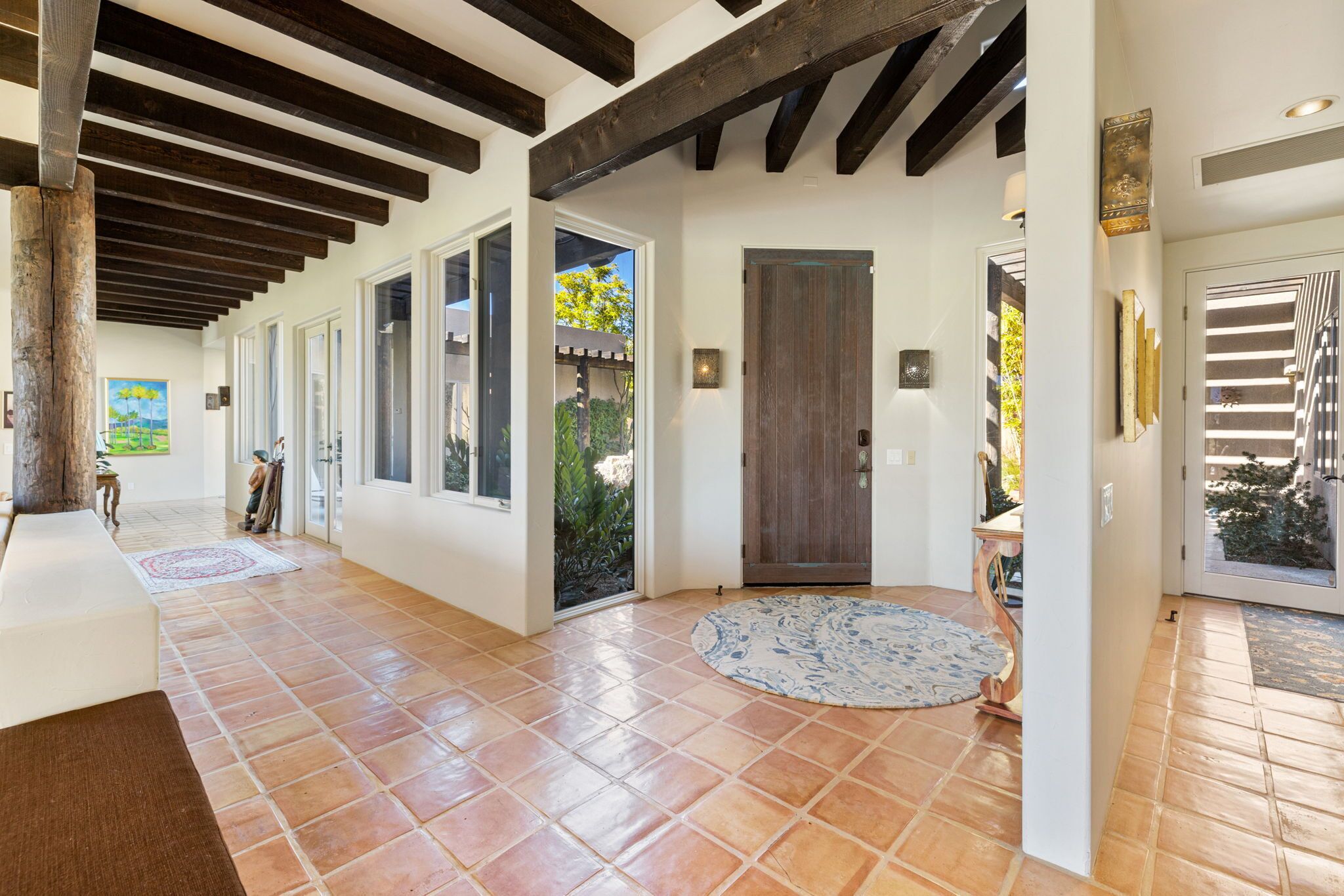 A spacious hallway with tiled flooring, wooden beams, and a large wooden door.