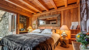 Une chambre confortable avec un grand lit, des poutres en bois, des murs en pierre et une cheminée en pierre.