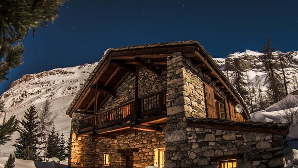 Une cabane en pierre dotée d’un balcon en bois, entourée de neige et d’arbres.