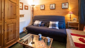 Um quarto aconchegante com um sofá azul escuro, um guarda-roupa de madeira e uma mesa de centro de vidro com um livro e duas canecas.
