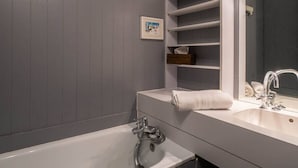 Uma casa de banho moderna com uma banheira branca, um espelho grande e prateleiras embutidas para toalhas e produtos de higiene pessoal.