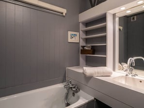 Ein modernes Badezimmer mit einer weißen Badewanne, einem großen Spiegel und eingebauten Regalen für Handtücher und Toilettenartikel.