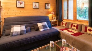 Quarto de cabana aconchegante com um sofá azul escuro, uma mesa de centro de vidro e uma cama com almofadas da bandeira do Canadá.