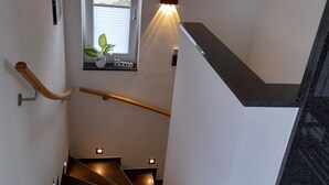 Una escalera moderna con barandilla, un ventanal con planta y un aplique de pared.