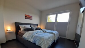 Un dormitorio con cama, mesitas de noche, un cuadro y una puerta corrediza al exterior.