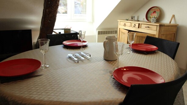 A dining table set with red plates, clear glasses, and cutlery, with a view of a window and a wooden cabinet in the background.