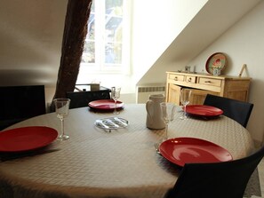 A dining table set with red plates, clear glasses, and cutlery, with a view of a window and a wooden cabinet in the background.