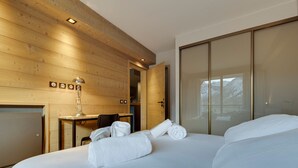 A modern hotel room with a large bed, a desk with a lamp, and a wardrobe.