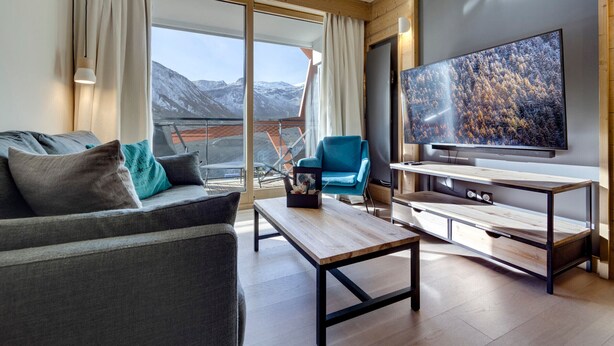 A modern living room with a sofa, a coffee table, a TV, and a balcony with a mountain view.