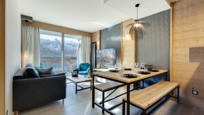 A modern living room with a sofa, a dining table set for four, and a large window with a view of mountains.