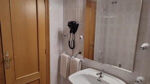 A bathroom with a wooden door, a white sink, a mirror with lights, and a hairdryer on the wall. - Hotel Novo (Ponferrada)