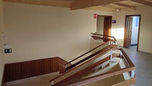 A wooden staircase with a handrail, a fire exit sign, and a door leading to another room. - Hotel Novo (Ponferrada)