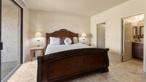 Un dormitorio con una cama grande, dos mesitas de noche con lámparas, un cabecero de madera y una puerta que da a otra habitación.