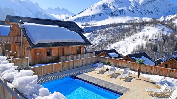 Una cabaña de madera con piscina y sillas de descanso, rodeada de montañas nevadas.