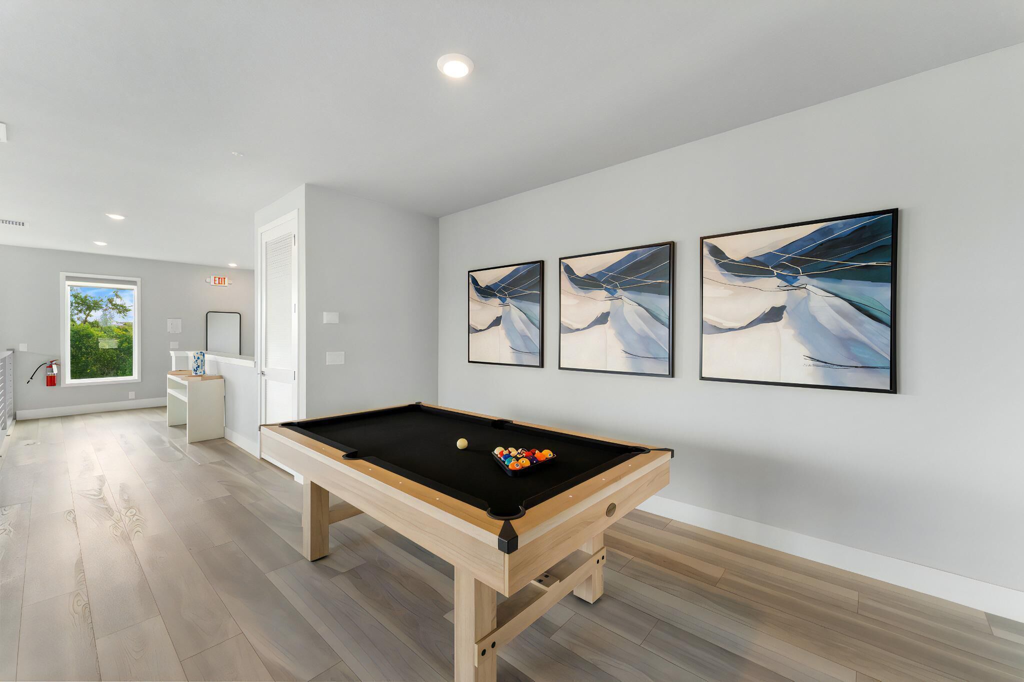 A pool table in a room with white walls and wooden flooring. There are three framed artworks on the wall.