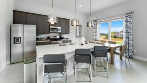 A modern kitchen with stainless steel appliances, a central island with bar stools, and large windows offering a view of the outdoors.