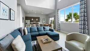 A modern living room with a sectional sofa, a coffee table, and a chair. There is a kitchen in the background with a dining area.