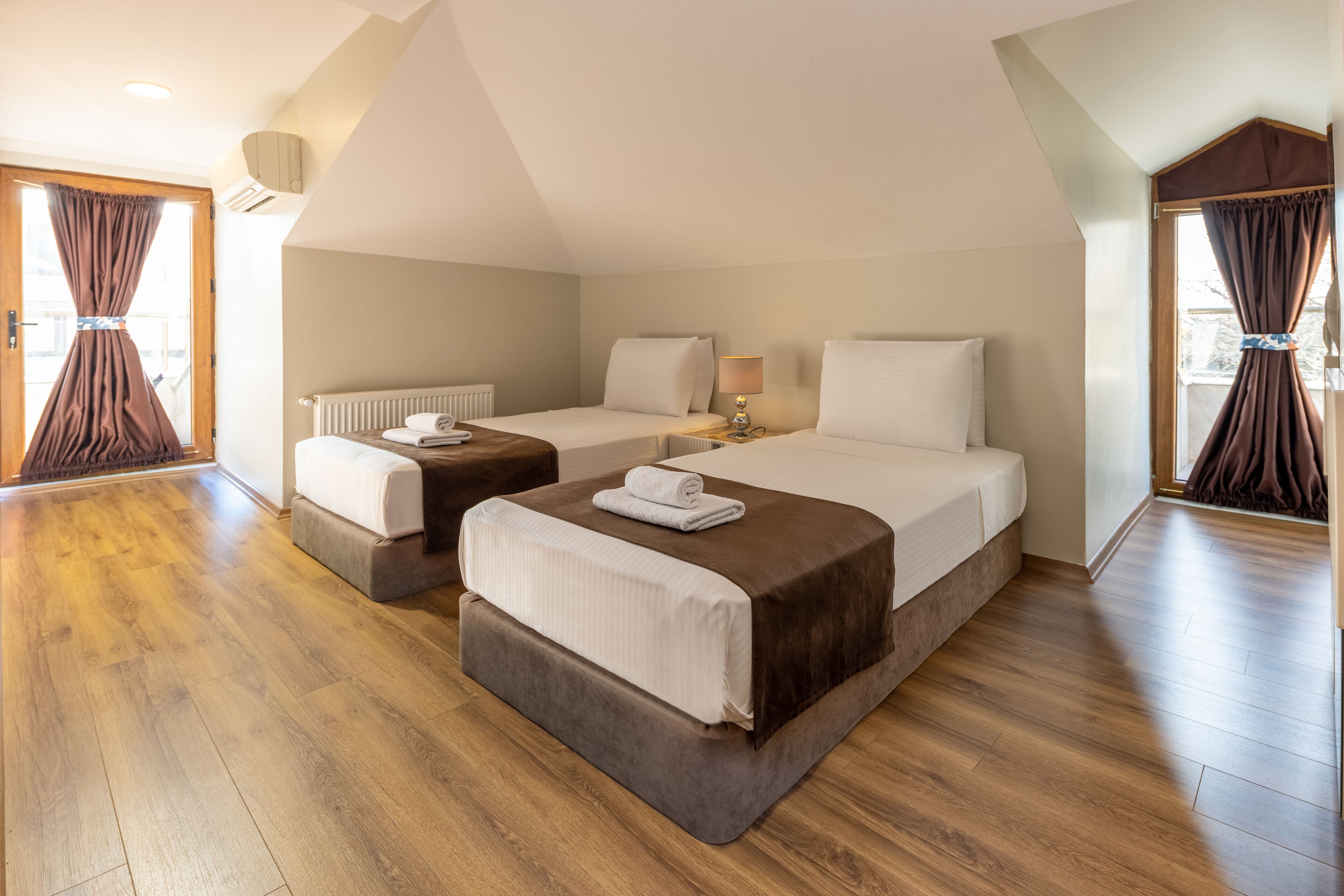 Une chambre d’hôtel avec deux lits, un plancher en bois, un radiateur et une fenêtre avec des rideaux.