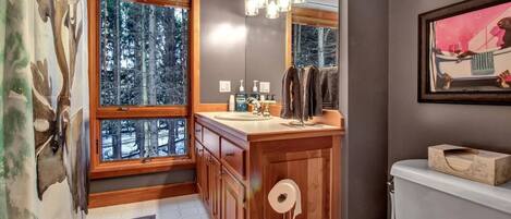 A bathroom with wooden cabinets, a sink, a toilet, and a window with a view of trees.